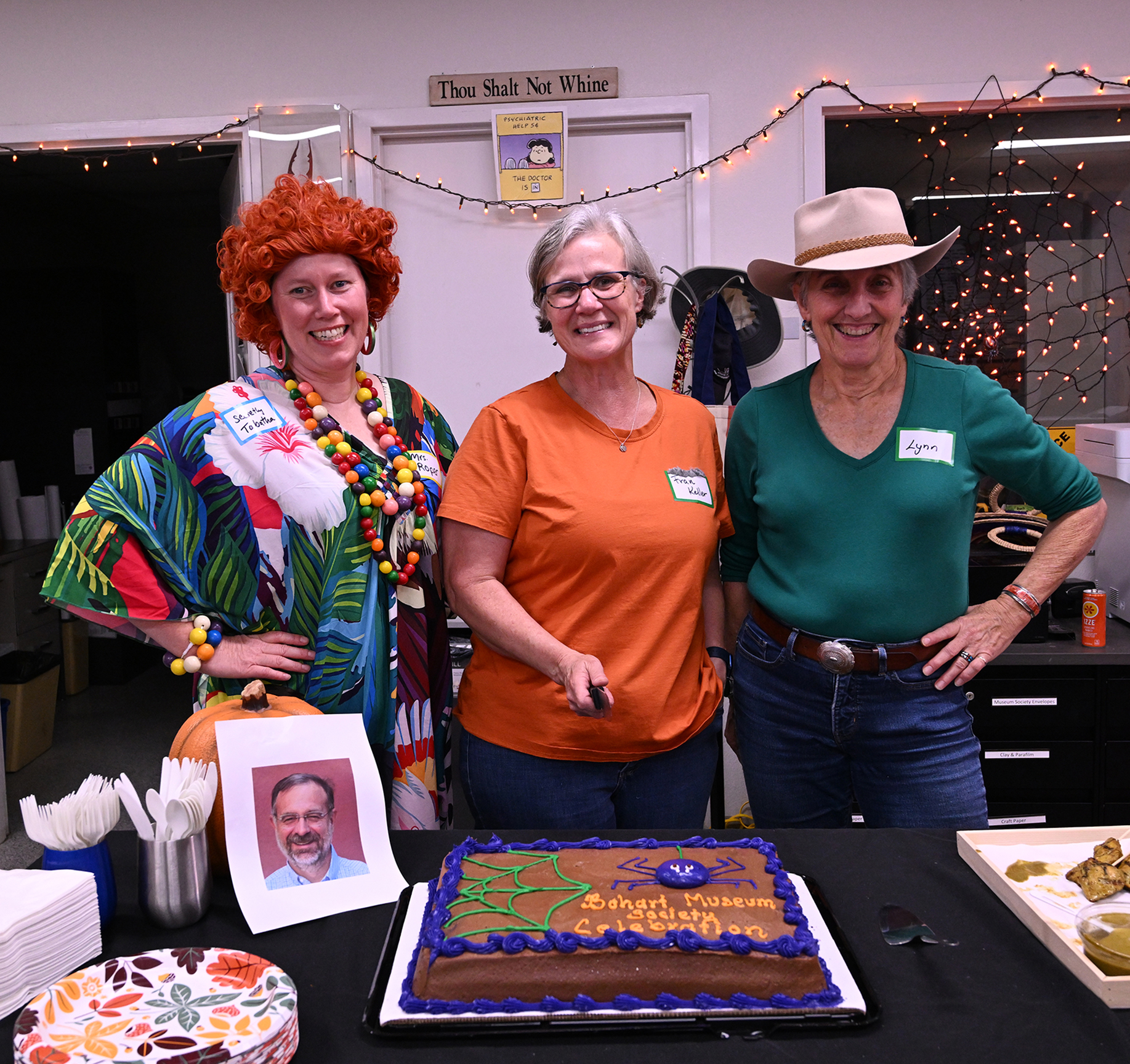Ready to cut the Bohart Museum Society's Halloween cake at the Bohart Museum of Entomology are Tabatha Yang, education and outreach coordinator; Professor Fran Keller of Folsom Lake College and a UC Davis entomology lecturer; and UC Davis Distinguished Emerita Lynn Kimsey, who heads the Bohart Museum Society. Also pictured: an image of Bohart Museum director Jason Bond, who was in Africa doing research. The trio gave his image a piece of the spider cake. (Photo by Kathy Keatley Garvey)
