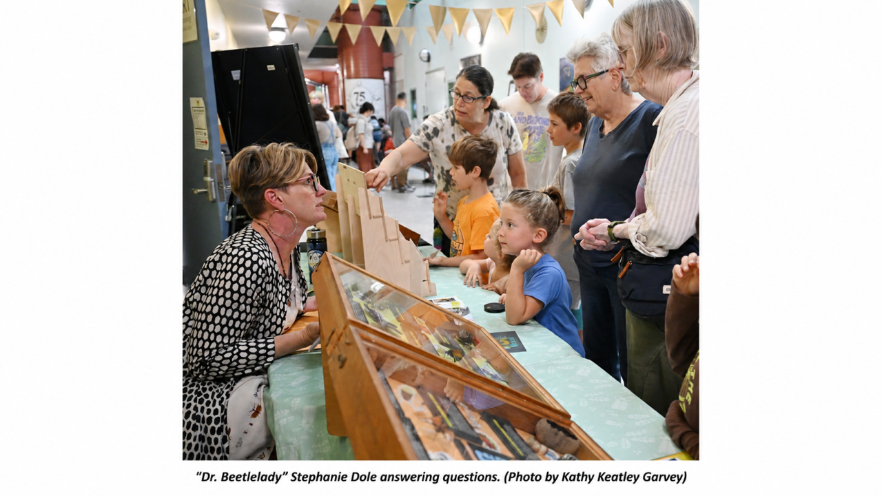 Children and adults gathered around a museum display case, Stephanie Dole pointing at artifacts.  