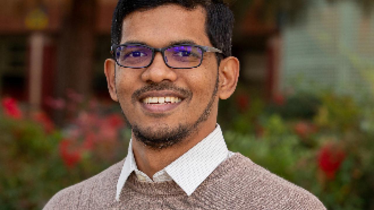Portrait photo of smiling man with glasses and beard in garden wearing brown sweater