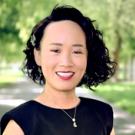 Smiling woman portrait with short curly hair, black dress and necklace, tree-lined path