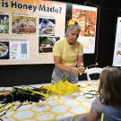 Woman in yellow making bee crafts at a honey exhibit, child watching